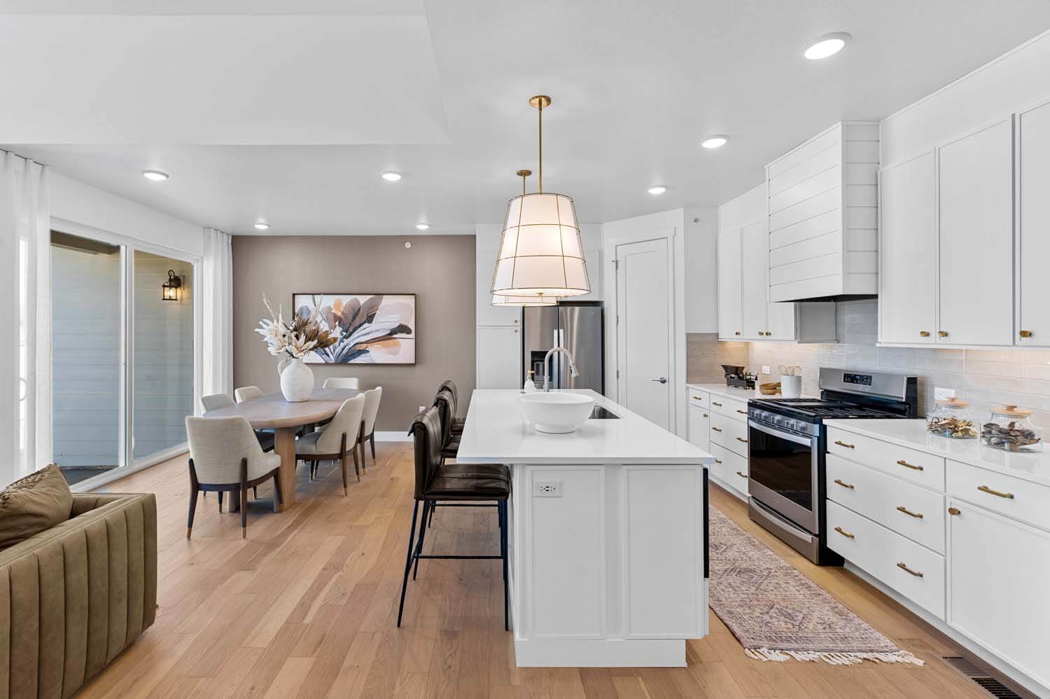 The long, white quartz island is between the dining area and the white kitchen cupboards and counters.