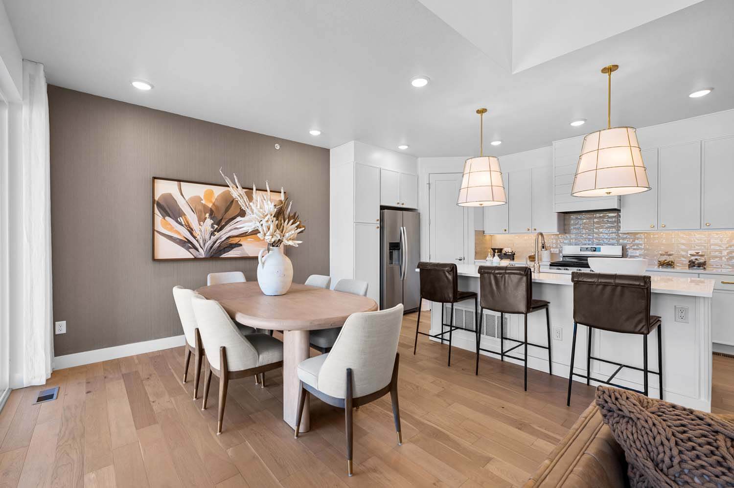 The open design of the main floor has the dining area, with its tan wallpapered accent wall, next to the kitchen featuring white cabinets, quartz counters and stainless steel appliances.