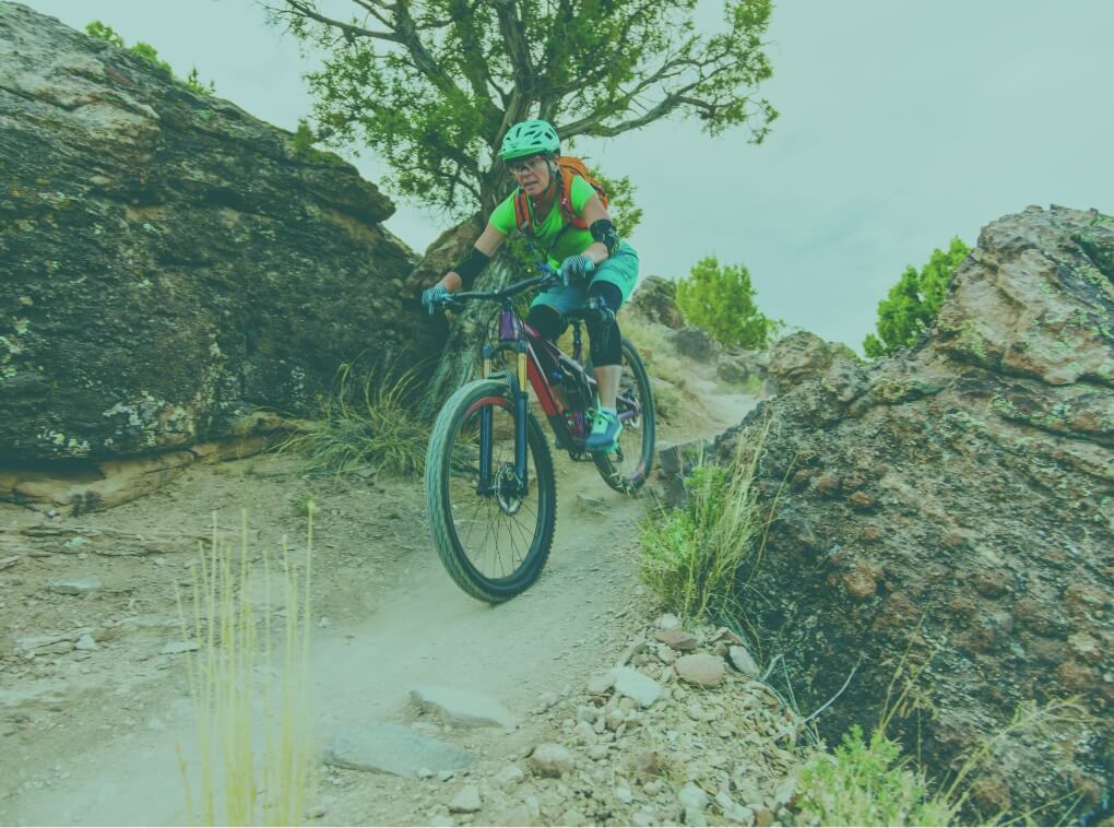 A person rides a mountain bike down a trail surrounded by rocky terrain.