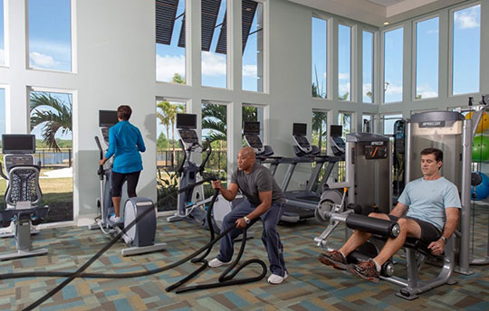 Three people exercising in a workout room with large windows to the ceiling on both walls
