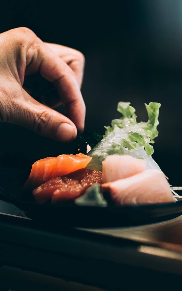A hand reaching toward a plate of sushi