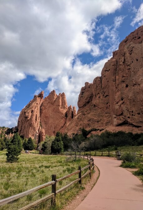A paved path lined by fences on either side, runs along the Red Rocks.